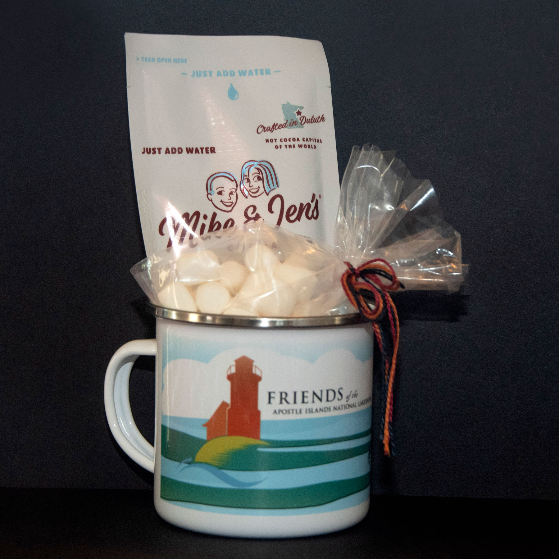 Enamel mug featuring the Friends of the Apostle Islands National Lakeshore logo set against a colorful background of blue, green and white